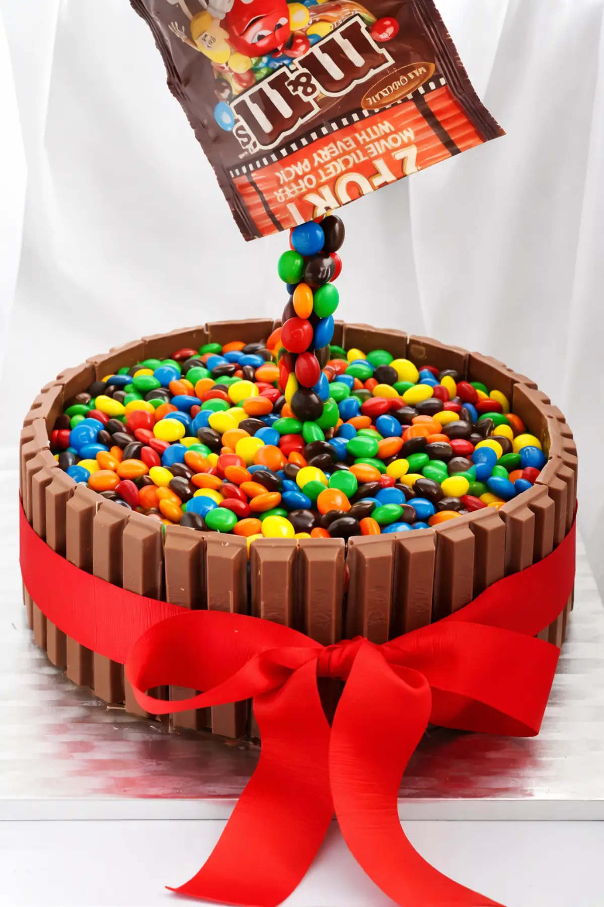 Colourful chocolate candies forming a suspended stream above a cake bordered with Kit Kat bars.
