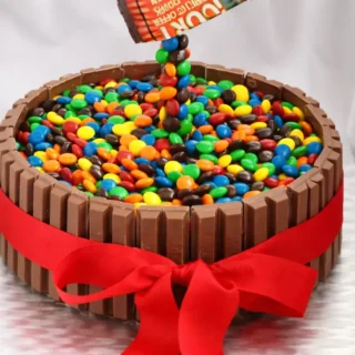 Close-up of M&M’s forming a gravity effect on a Kit Kat cake with a flowing candy stream.