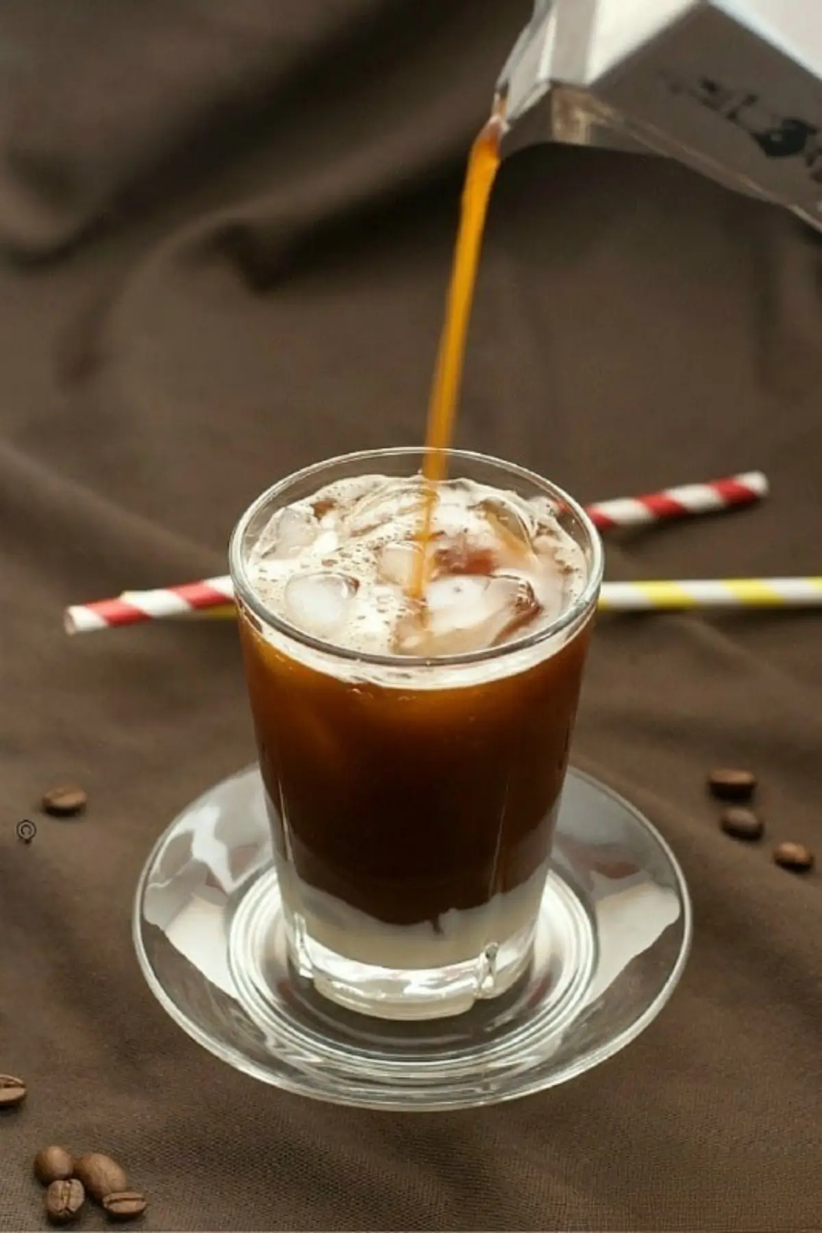 Hot coffee poured over ice and condensed milk in a glass.