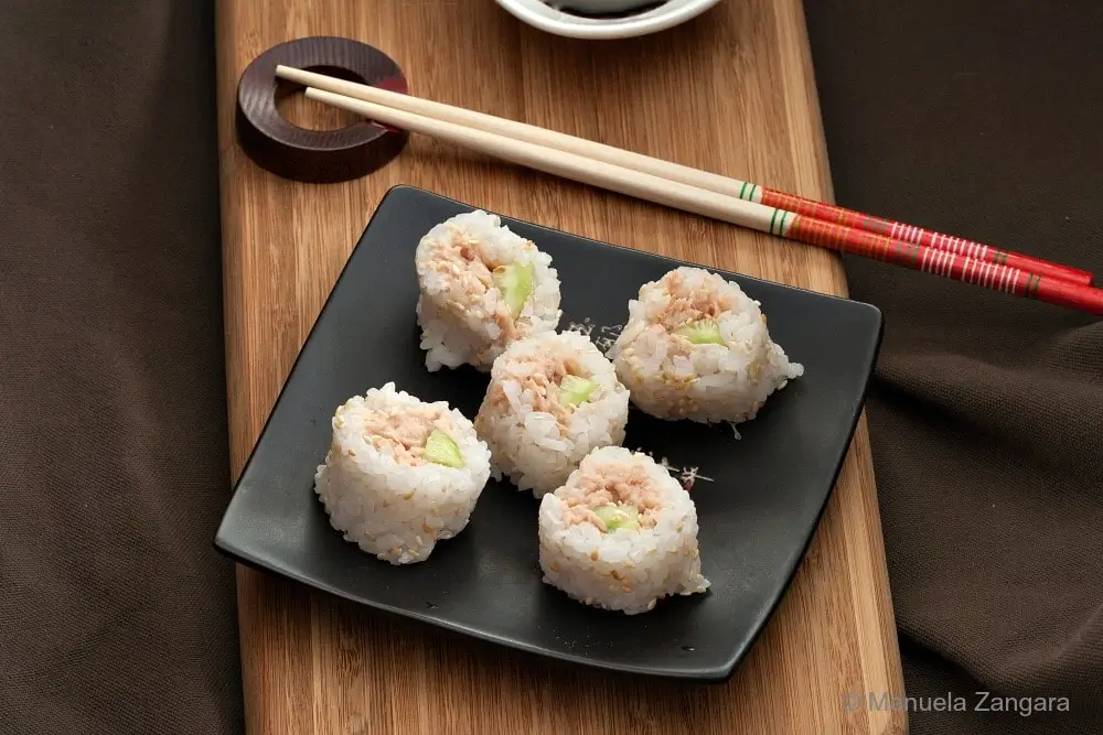 Close-up of tuna sushi rolls served on a black plate with chopsticks.