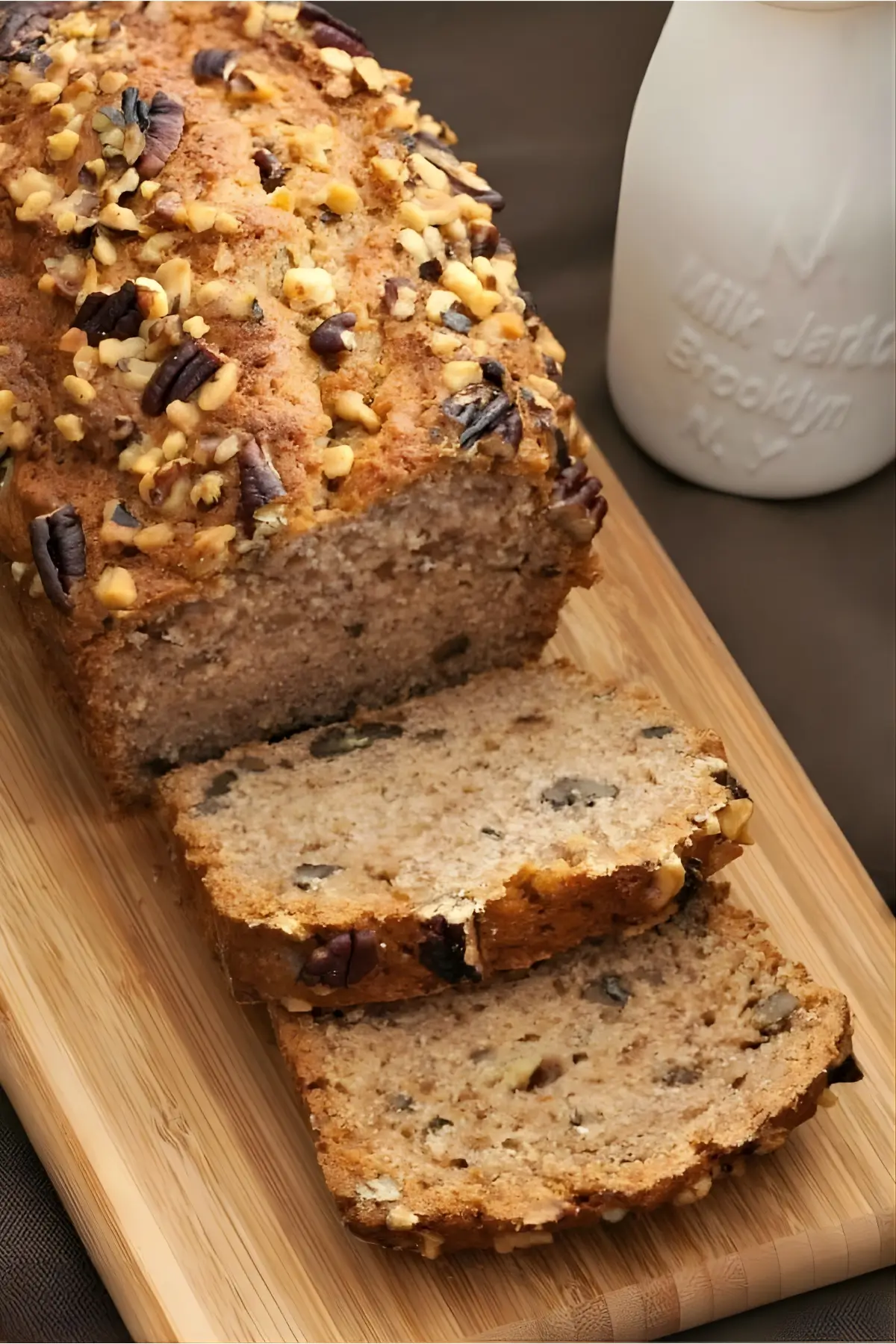 Sliced Copycat Starbucks Banana Nut Bread on a wooden board beside a milk jar.