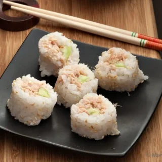 Six tuna sushi roll pieces arranged on a black plate over a wooden board.