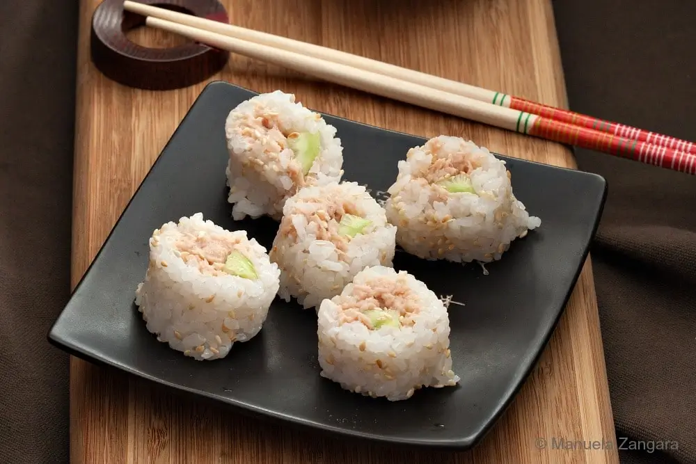 Six tuna sushi roll pieces arranged on a black plate over a wooden board.