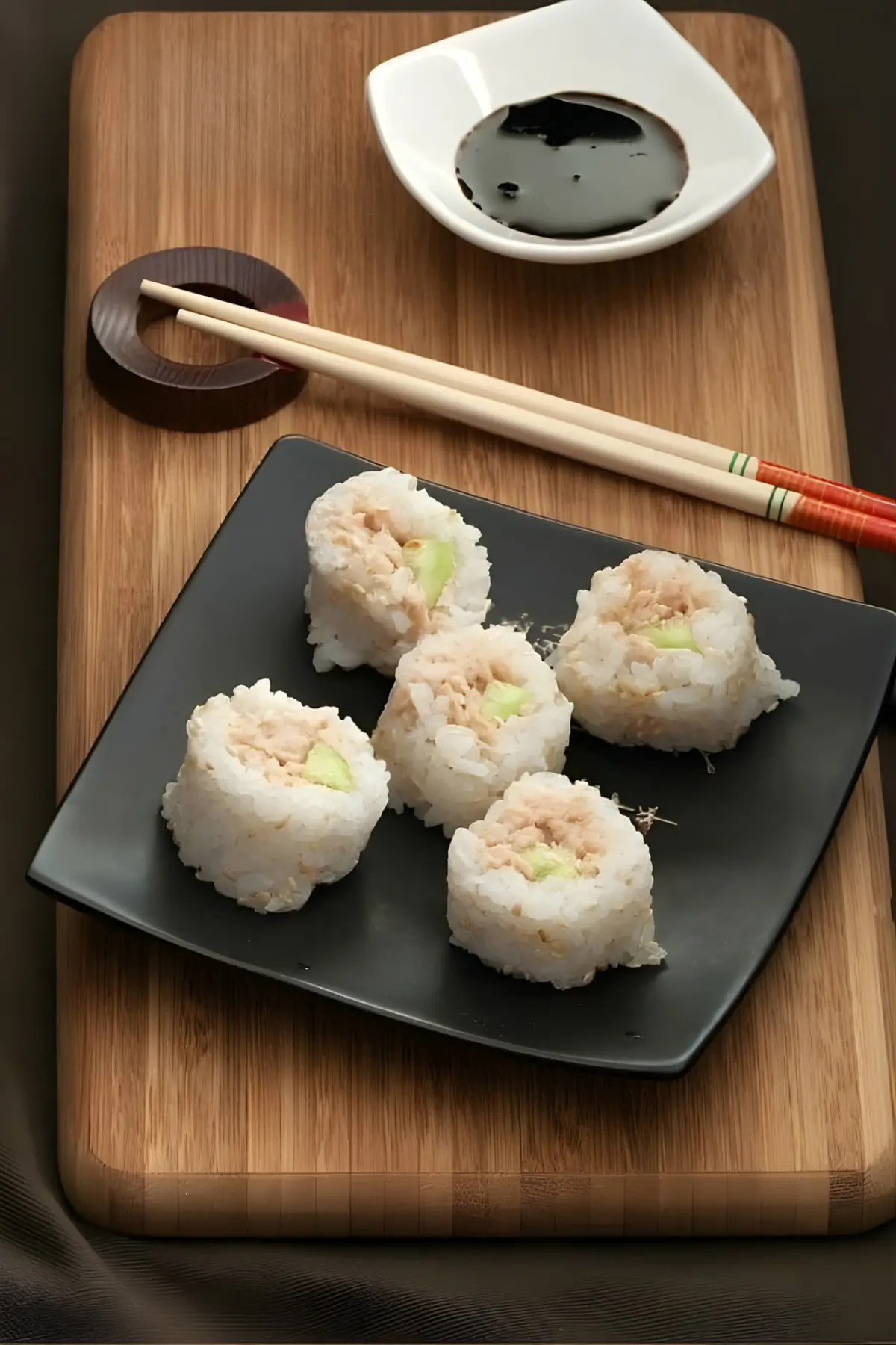 Sliced tuna sushi rolls on a black plate with soy sauce on the side.