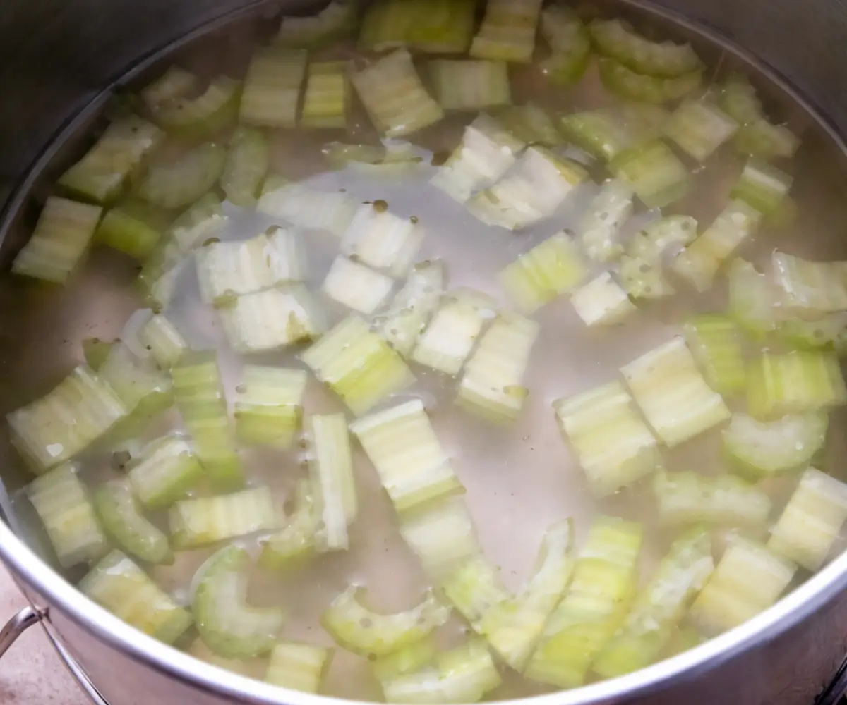 Chopped celery pieces blanching in lightly salted boiling water inside a large saucepan.
