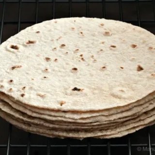 A stack of cooked wholemeal chapatis cooling on a rack.