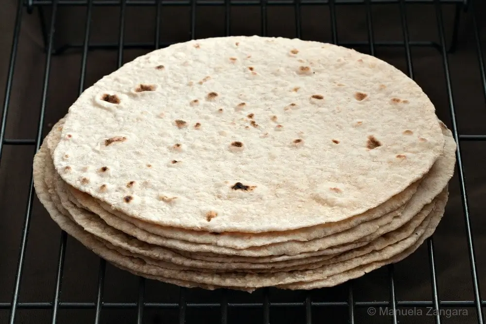 A stack of cooked wholemeal chapatis cooling on a rack.