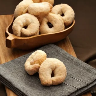 Sweet Taralli arranged in a wooden bowl with a few biscuits placed on a folded napkin.
