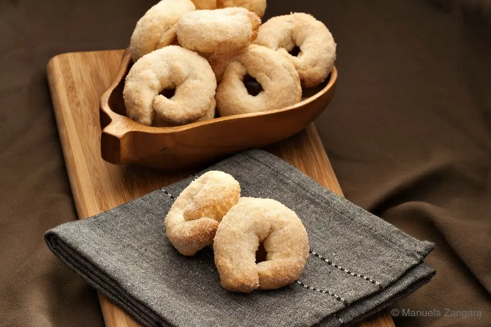 Sweet Taralli arranged in a wooden bowl with a few biscuits placed on a folded napkin.