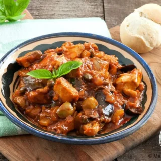 Swordfish Caponata served in a rustic bowl with fresh basil and warm bread on the side.