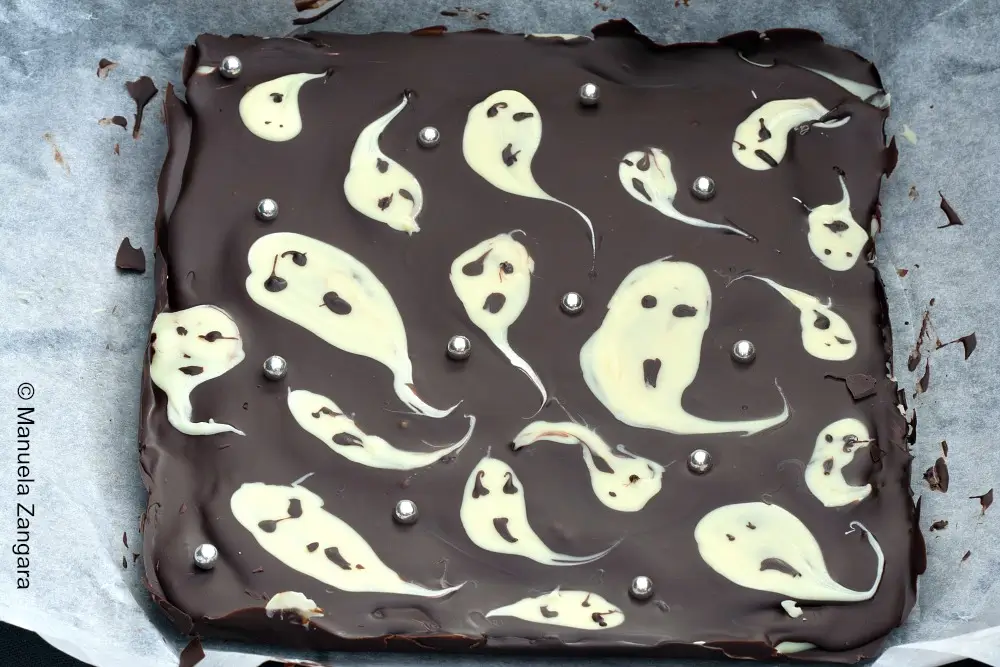 Square slab of Ghastly Bark decorated with white chocolate ghosts and silver pearls on a baking tray.