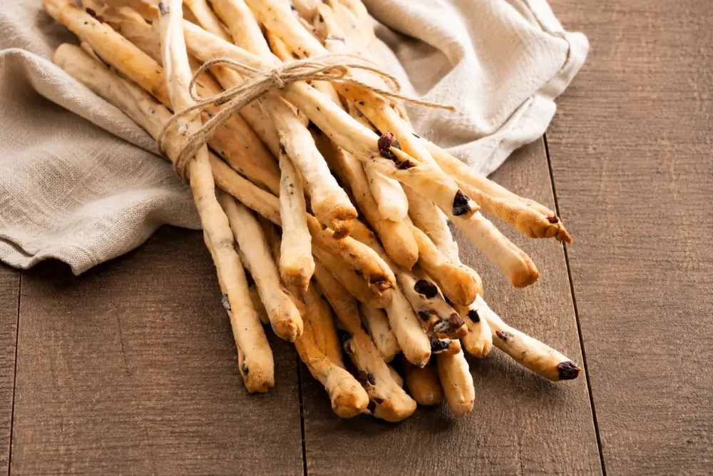 Rustic bundle of olive breadsticks resting on a linen cloth over a wooden table.