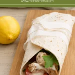 Lemon chicken wrap with aioli, tomato and rocket served on a wooden board.