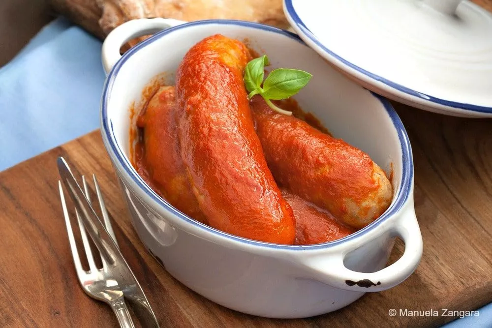 Close-up of Italian sausages in thick tomato sauce, garnished with fresh basil.