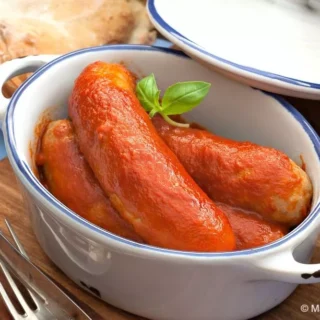 Italian sausages in rich tomato sauce inside a white casserole.