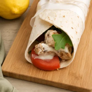 Lemon chicken wrap with aioli, tomato and rocket served on a wooden board.