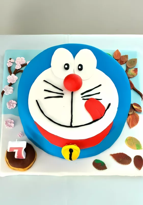 Doraemon fondant cake with red collar, yellow bell, and number 7 candle.