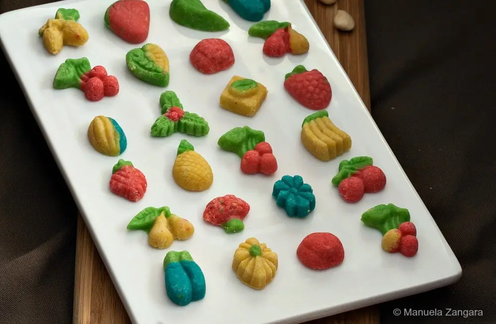 Assorted colourful Goan marzipans shaped like fruit and displayed on a white platter.