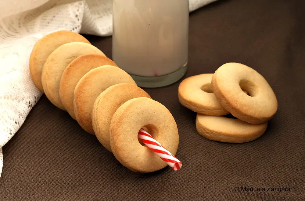 Macine cookies arranged on a table with a bottle of milk in the background.