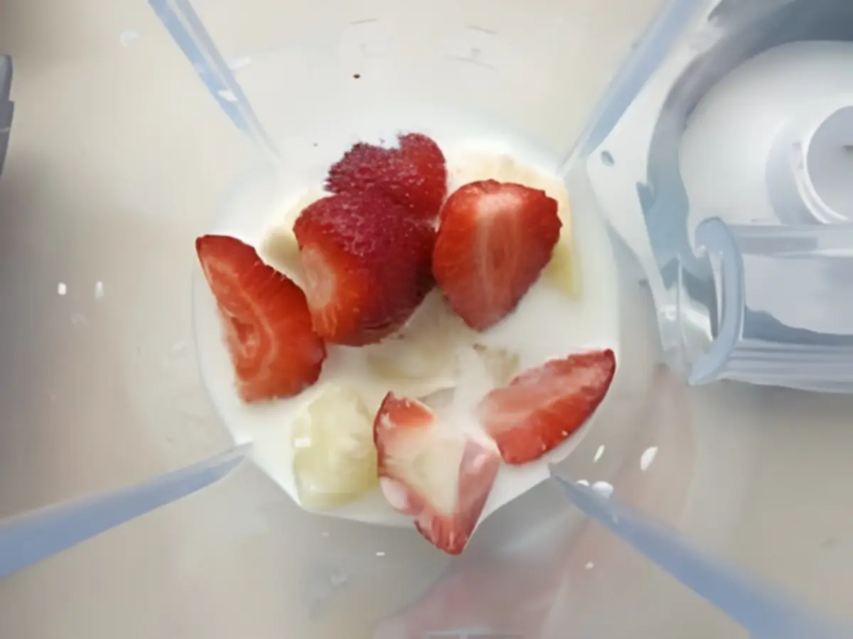 Strawberries, pineapple, apple, and milk added to a blender.