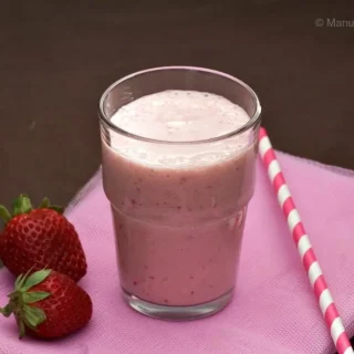 Pineapple strawberry apple smoothie with striped straw on plate.