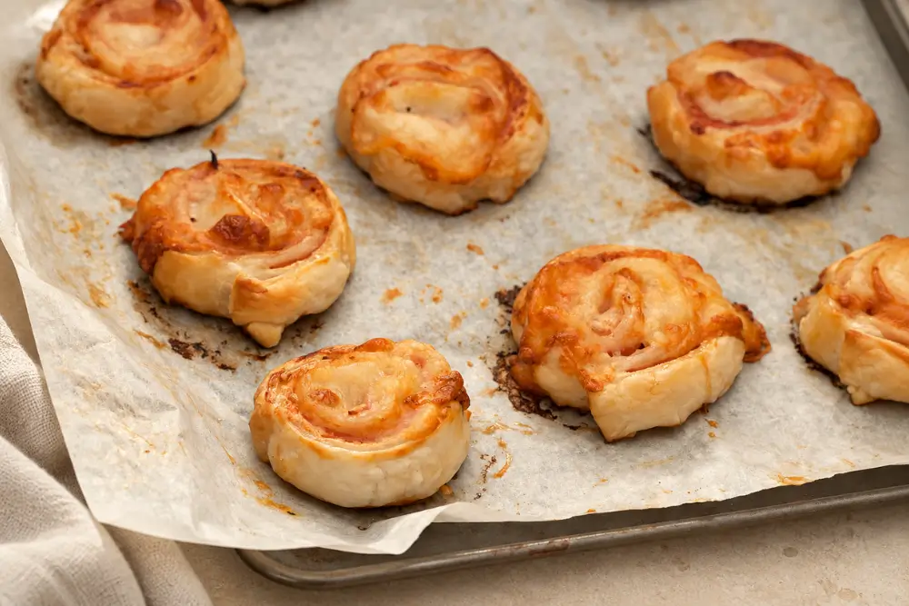 Baked cheese and ham pinwheels arranged on a parchment-lined tray.