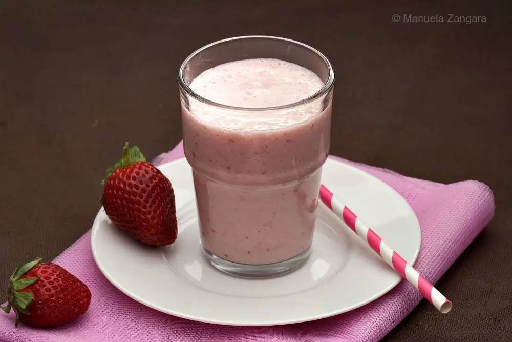 Pineapple strawberry apple smoothie served with fresh strawberries.