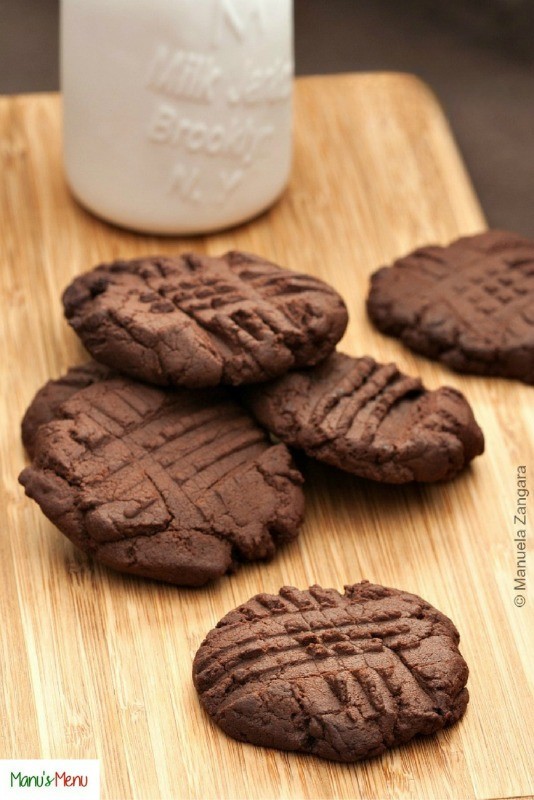 Stack of chocolate buttercream cookies served with a bottle of milk on a wooden board.