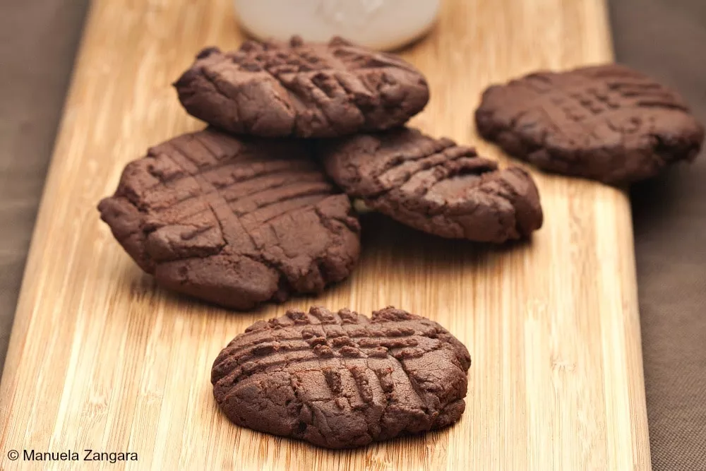 Freshly baked chocolate buttercream cookies cooling on a wooden board.