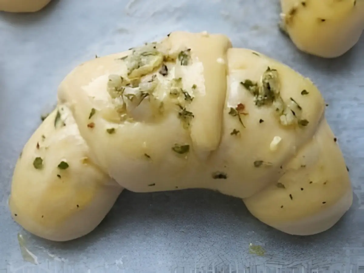 Unbaked croissant brushed with garlic and herb butter.