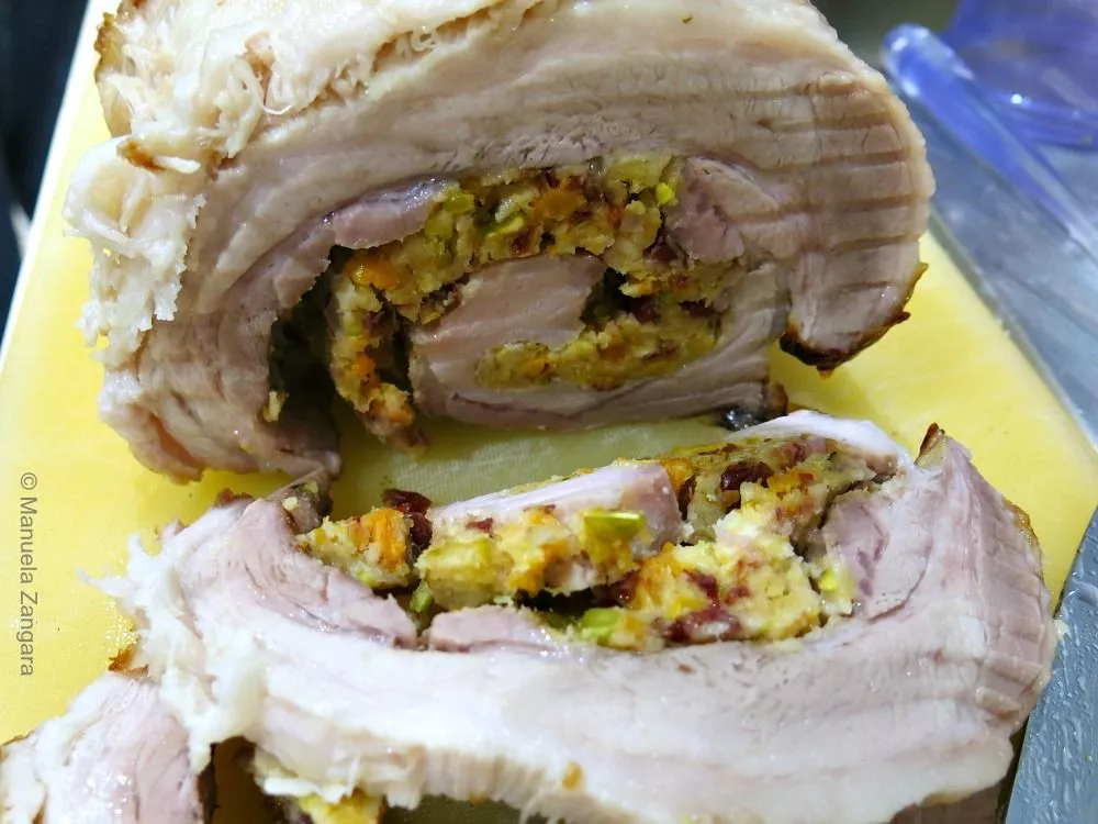 Sliced roast pork with fruit and nut stuffing showing juicy layers of meat.