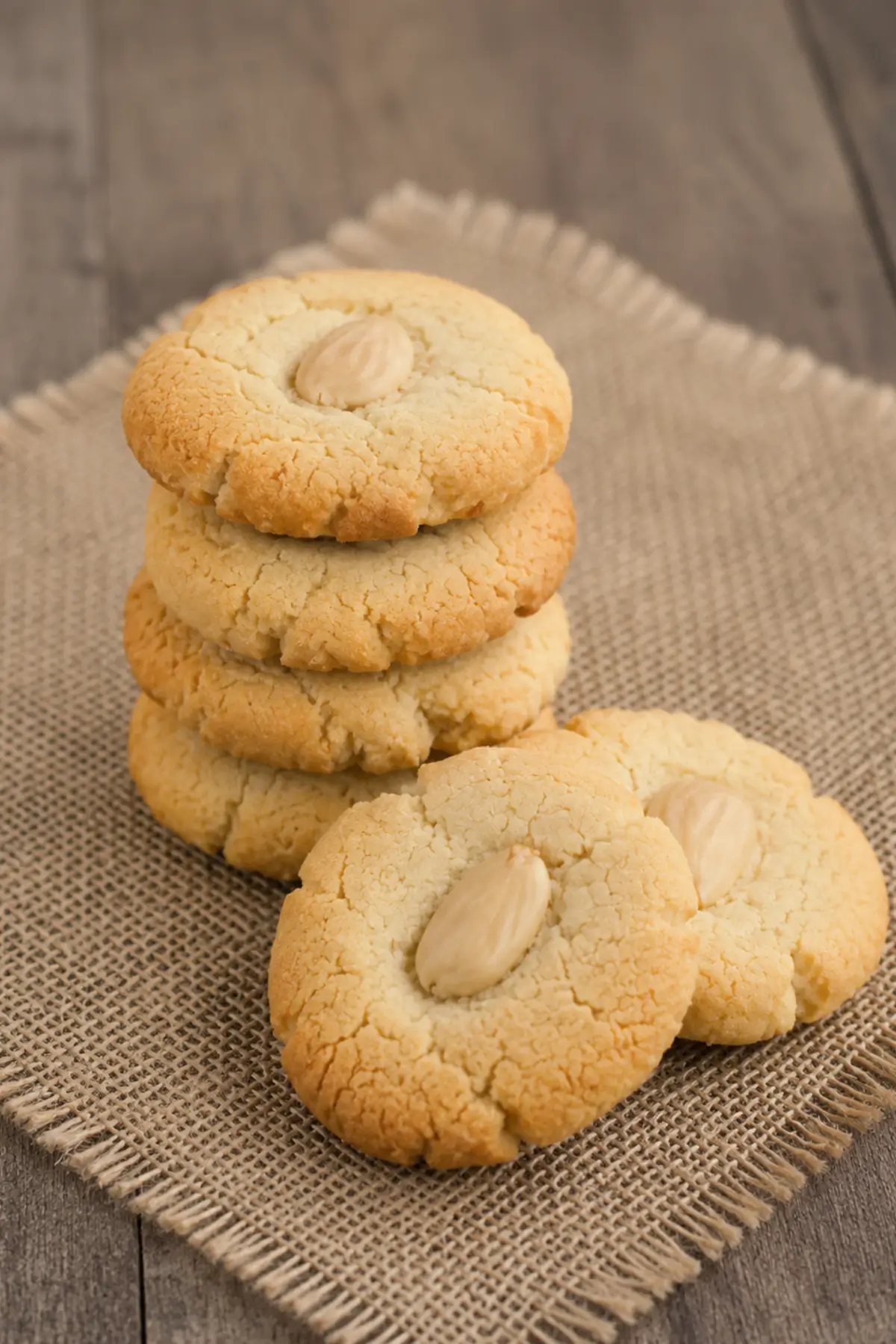 Stacked almond cookies with whole almond toppings on a cloth-lined surface.
