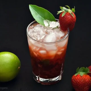 Strawberry Caipiroska cocktail with crushed ice, fresh strawberries, and a whole lime on the side.