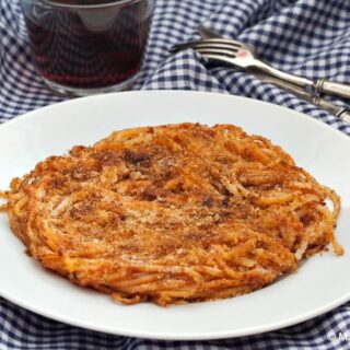 Close-up of a crispy fried spaghetti cake on a white plate over a checkered cloth.