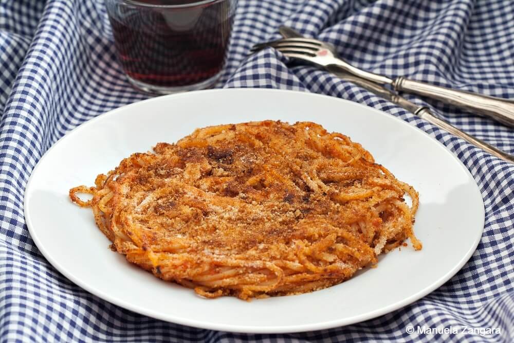 Close-up of a crispy fried spaghetti cake on a white plate over a checkered cloth.