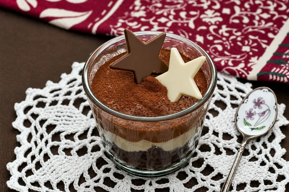Triple chocolate mousse layered with chocolate cake and topped with cocoa powder and chocolate stars in a glass dessert cup.