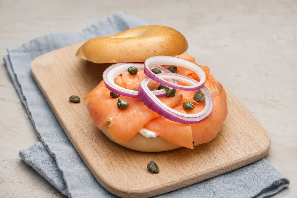 Open smoked salmon bagel topped with red onion rings and capers.