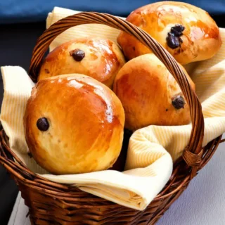 Freshly baked buns with a shiny glaze arranged in a lined basket.