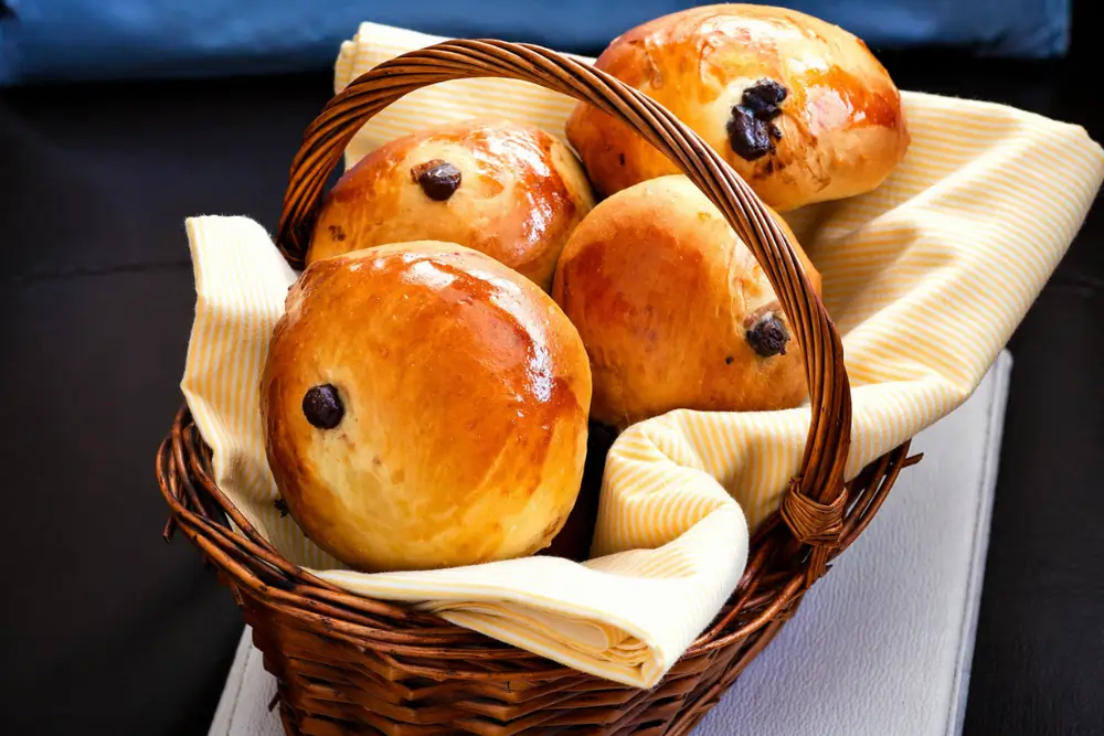Freshly baked buns with a shiny glaze arranged in a lined basket.