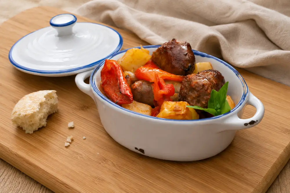 Italian pork sausage with golden potatoes and roasted red bell peppers in a white baking dish.