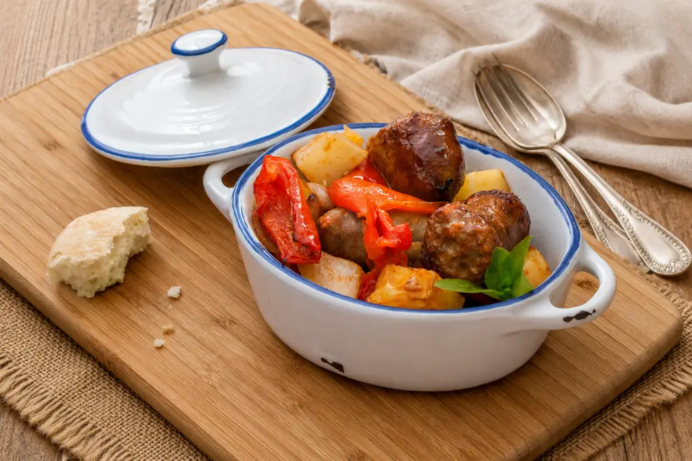 Italian Sausage with Bell Peppers served with golden potatoes in a white baking dish.