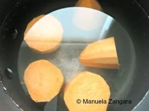 Sweet potato pieces simmering in a pot of water on the stove.