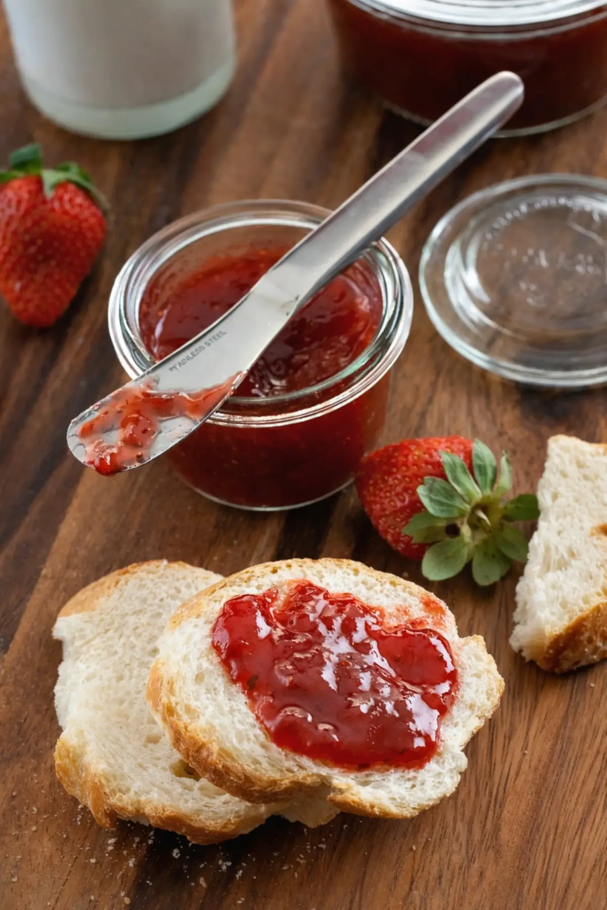 Strawberry jam spread on slices of bread with fresh strawberries nearby.