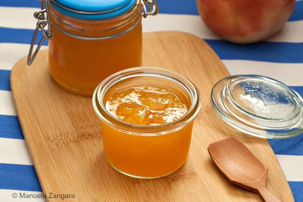 Glass jars filled with golden homemade peach jam on a wooden board.