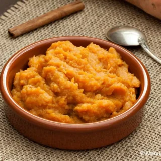 Homemade sweet potato mash in a ceramic bowl with a spoon on the side.