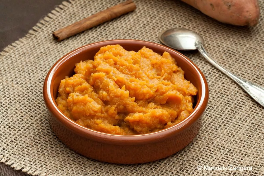 Homemade sweet potato mash in a ceramic bowl with a spoon on the side.