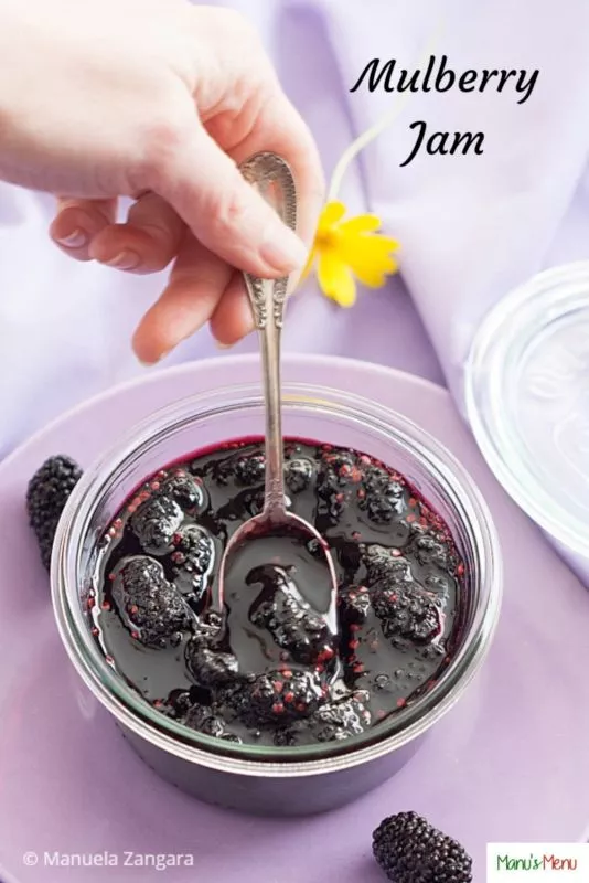 Thick mulberry fruit jam in a glass bowl with whole berries and a spoon.