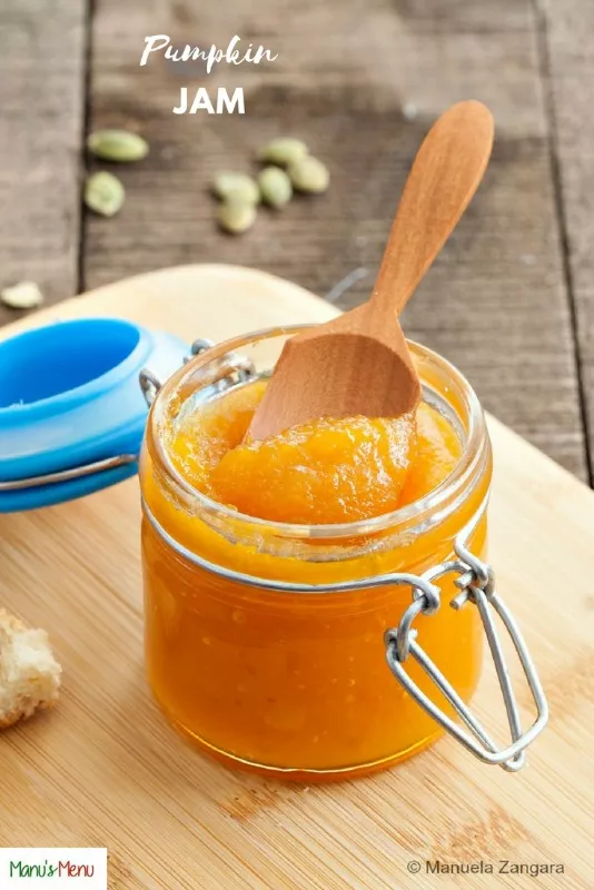 Bright orange pumpkin fruit jam in a small glass jar with a wooden spoon on top.