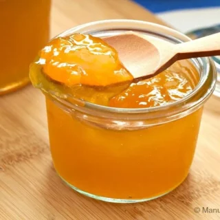 Close-up of a spoon lifting glossy homemade peach jam from a glass jar.
