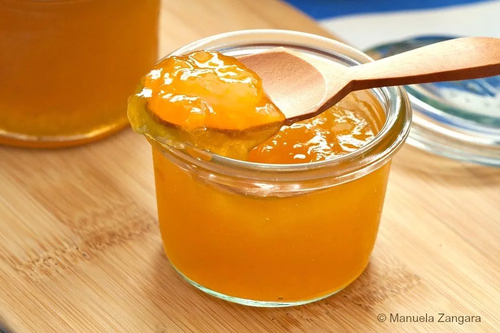 Close-up of a spoon lifting glossy homemade peach jam from a glass jar.